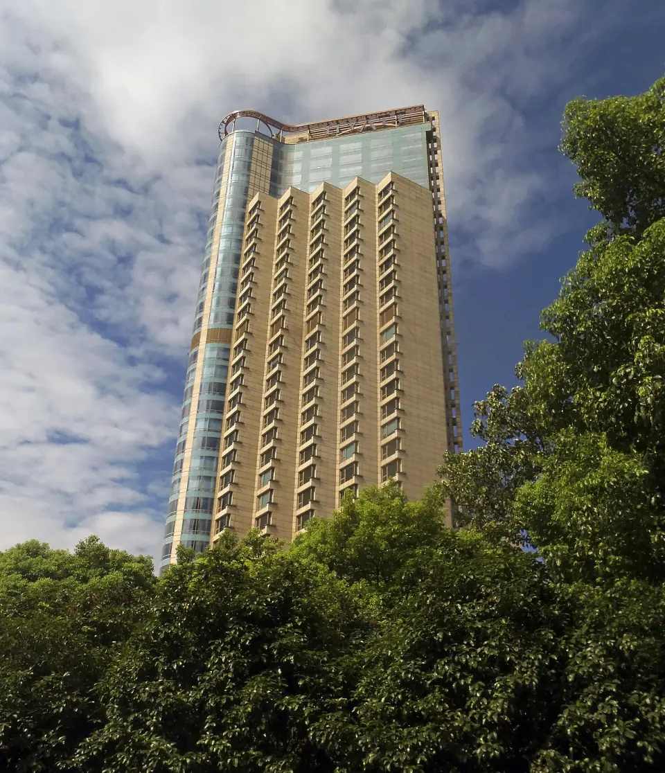 Hyatt on the Bund hotel tower above trees in Shanghai, photographed from street level