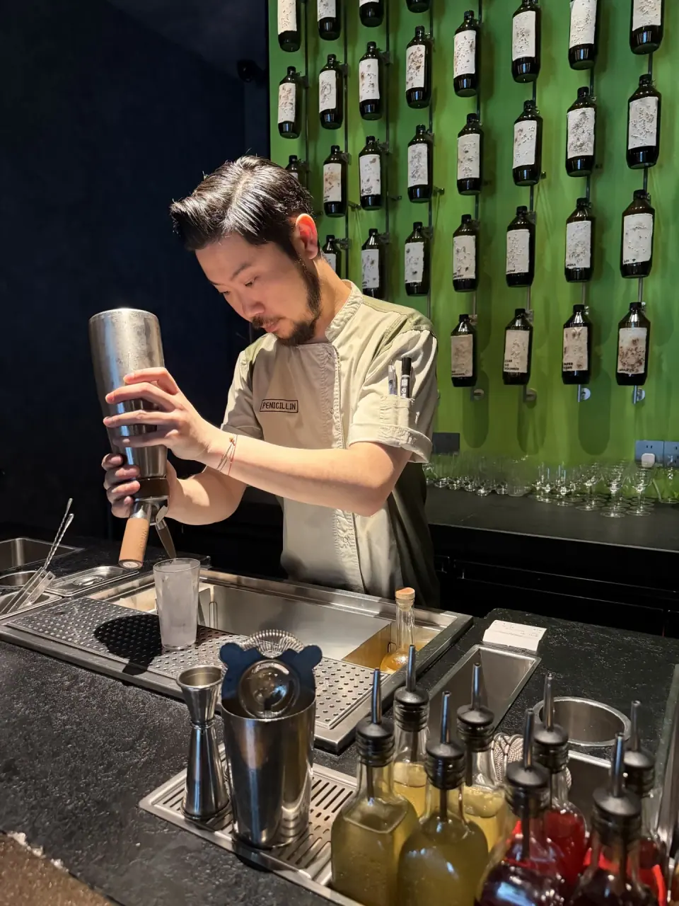 Bartender shaking a cocktail in front of a wall of bottles at Penicillin Shanghai